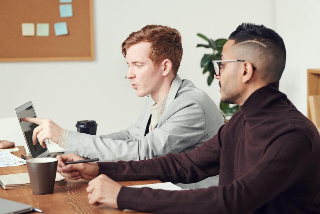 Two business professionals engaged in a collaborative discussion using a laptop in a modern office setting.