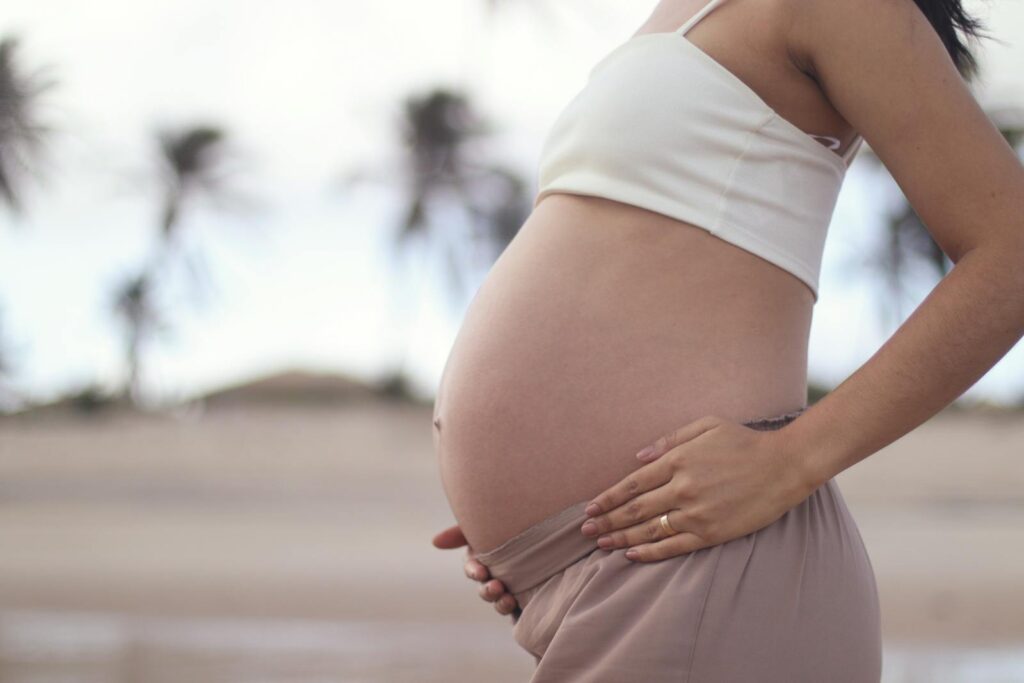 A serene portrait of a pregnant woman holding her belly at a tropical beach.