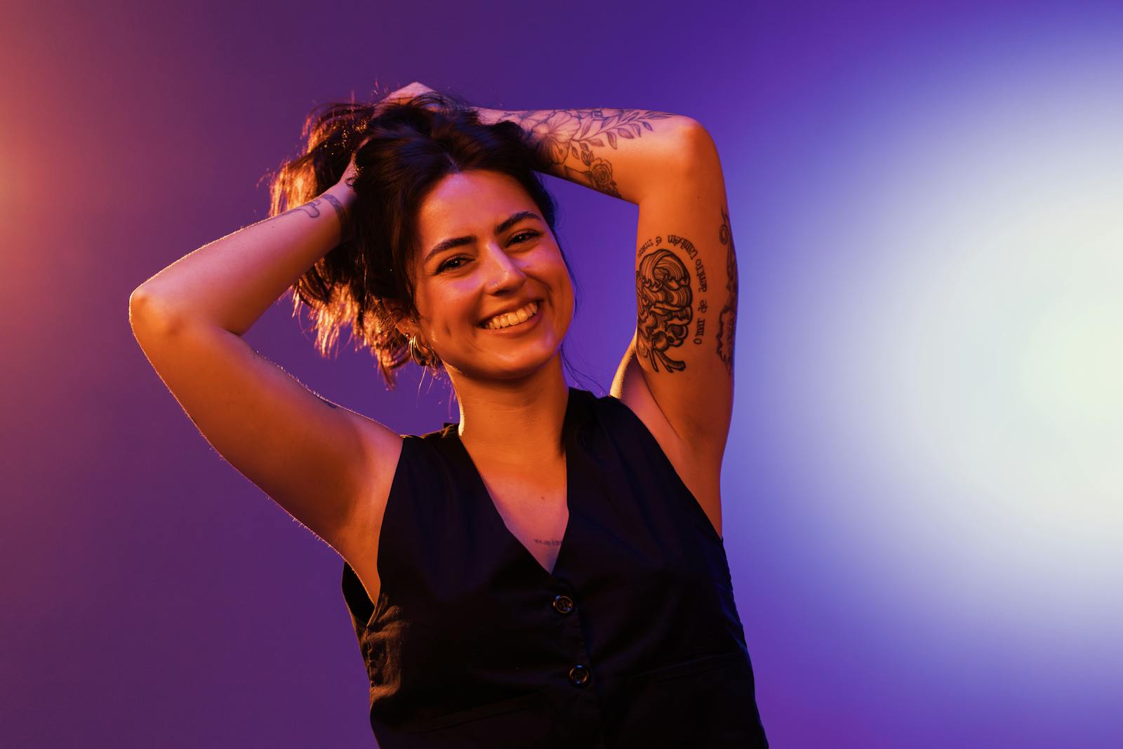 Joyful woman with tattoos posing in vibrant studio lighting, expressing happiness and style.