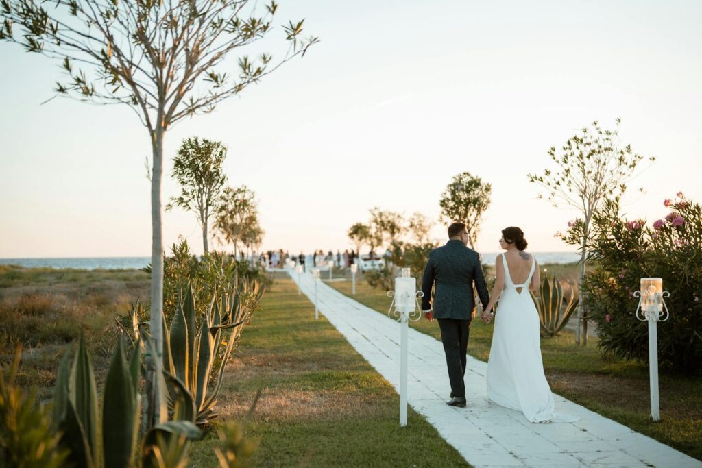 Couple walks hand-in-hand down aisle at outdoor beach wedding during golden hour.