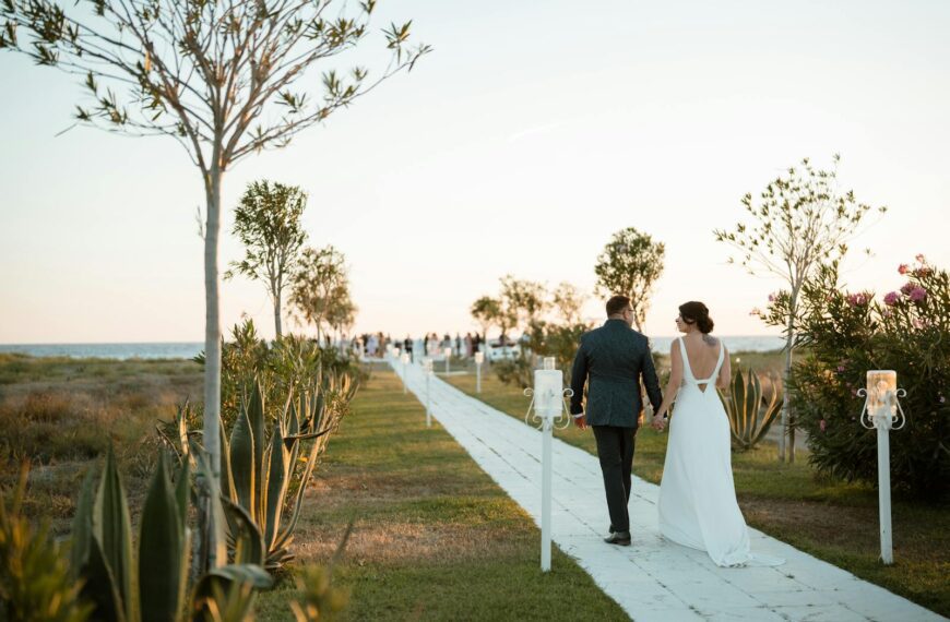 Couple walks hand-in-hand down aisle at outdoor beach wedding during golden hour.