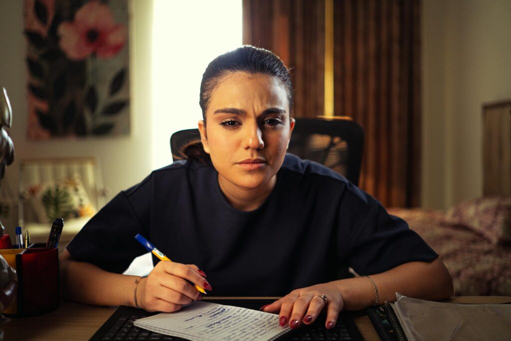 A woman intensely focused on writing notes at her home office desk, deep in concentration.