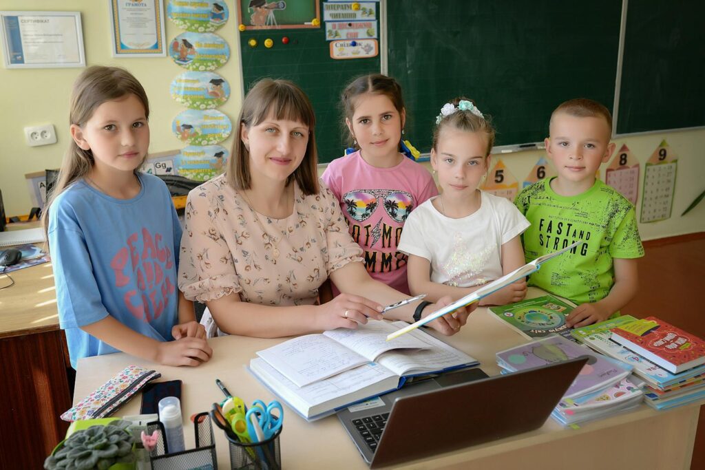 A teacher with four students in a classroom encouraging education and learning.