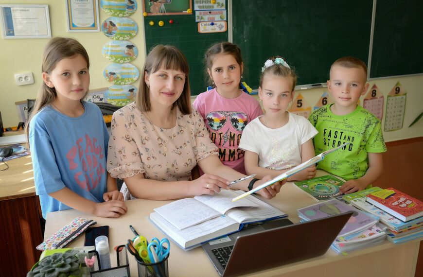 A teacher with four students in a classroom encouraging education and learning.
