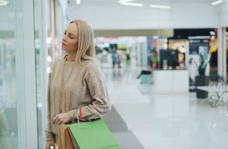 A woman carrying shopping bags looks at a store display in a modern mall.