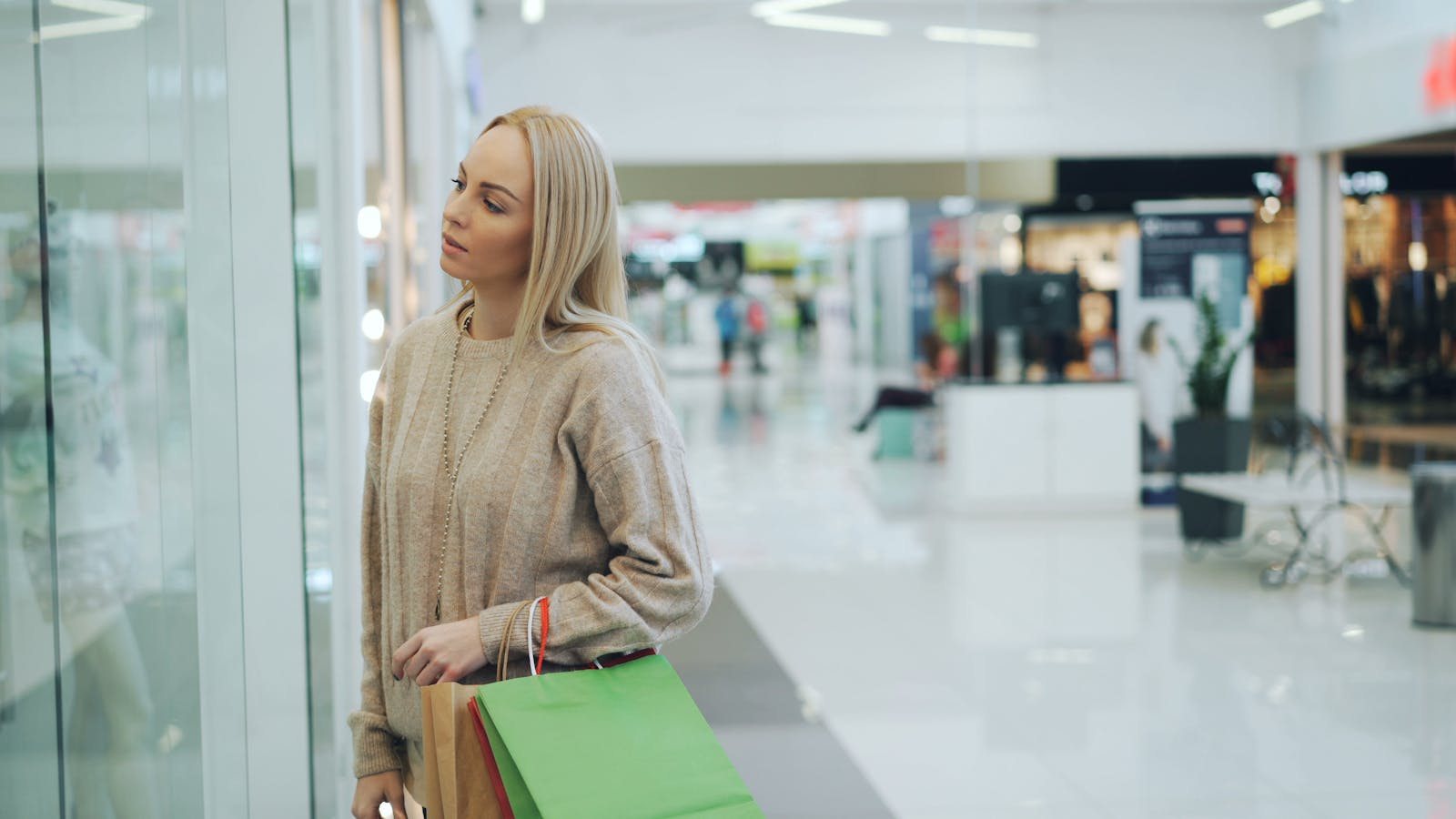 A woman carrying shopping bags looks at a store display in a modern mall.
