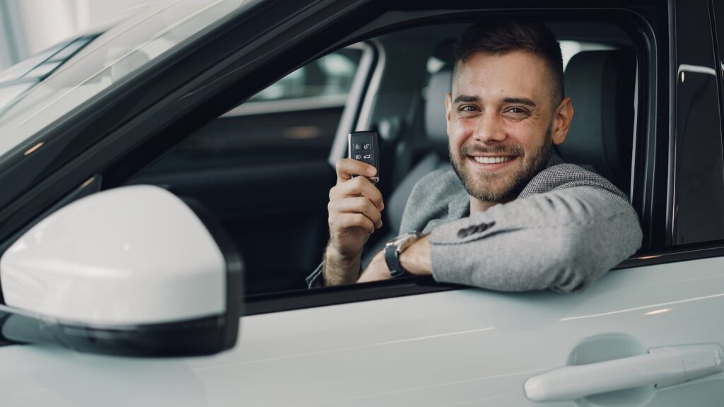 Happy young man holding car keys inside a vehicle. Perfect image for car rental or sales.