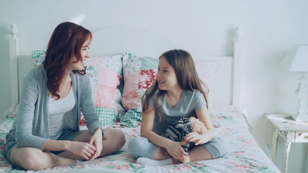 Smiling mother and daughter bonding on bed in cozy room.
