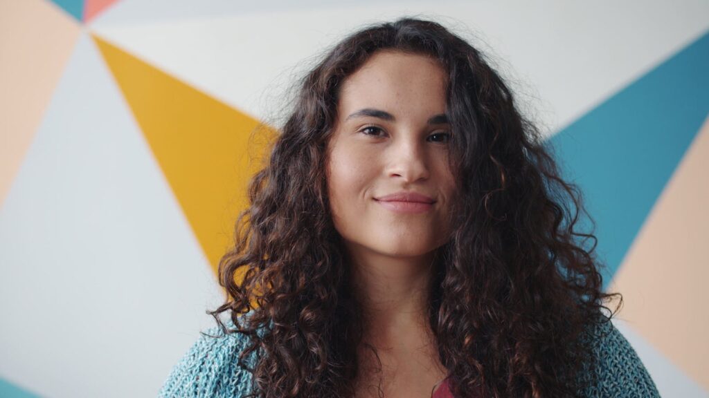 Close-up of a cheerful woman with curly hair against a geometric background. Vibrant and modern.
