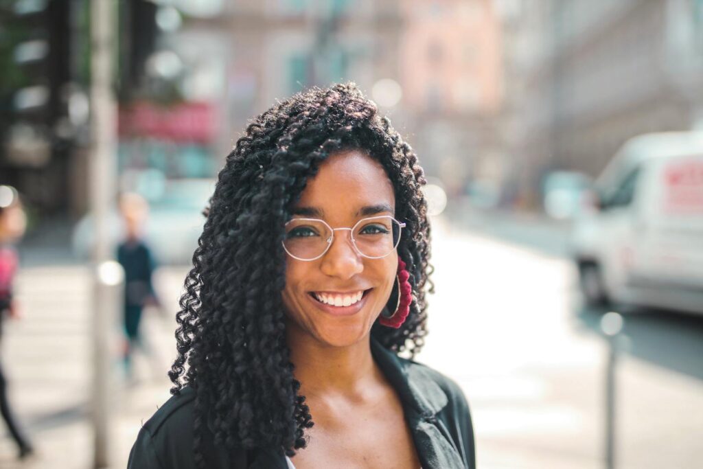 Attractive young woman with curly hair and eyeglasses smiling on a sunny day in the city.