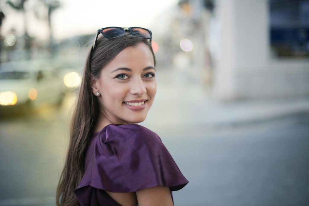 Cheerful woman in a purple top smiles at the camera on a bustling city street.