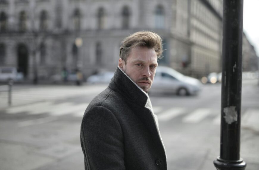 Side view of handsome male wearing classy jacket crossing road on sunny day and looking at camera
