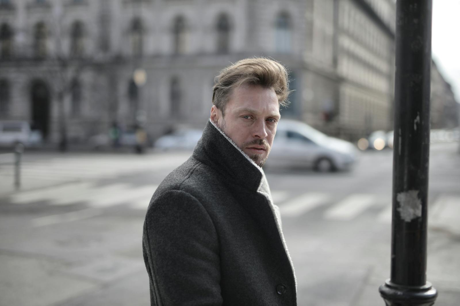 Side view of handsome male wearing classy jacket crossing road on sunny day and looking at camera