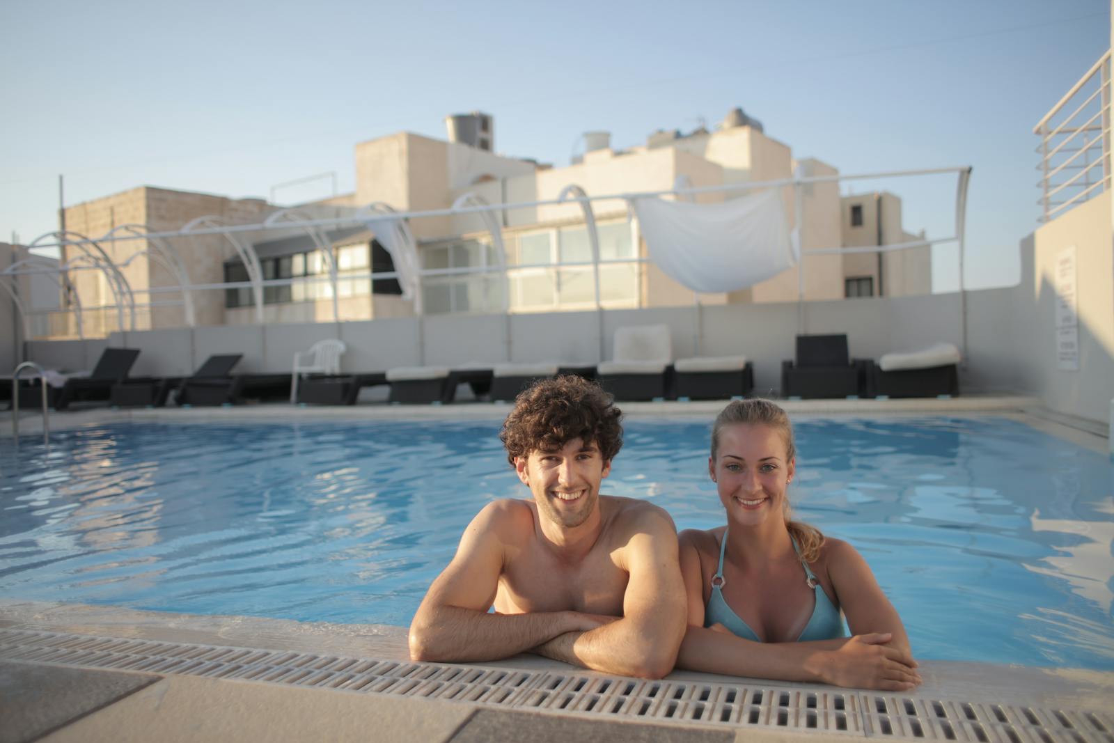 Happy young couple enjoying a sunny day at a tropical resort swimming pool.