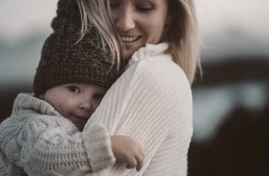 A tender moment of a mother embracing her child in cozy knitwear outdoors.