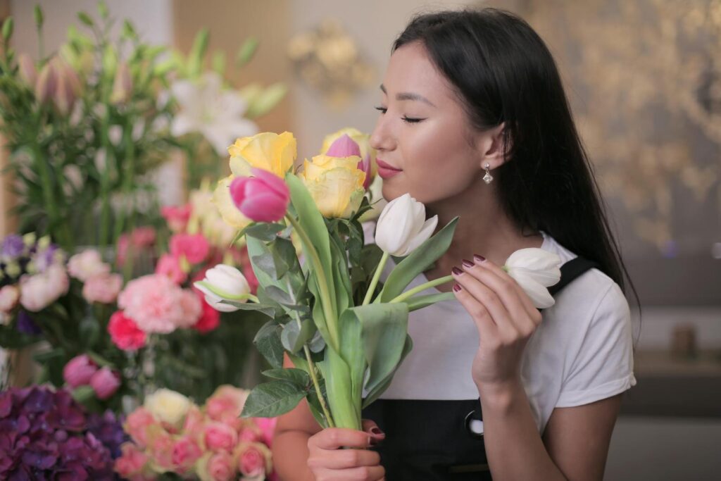 Asian woman admiring colorful tulips in a vibrant flower shop setting, embodying floral beauty.
