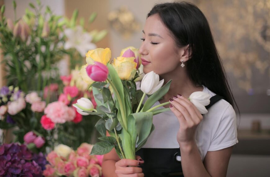 Asian woman admiring colorful tulips in a vibrant flower shop setting, embodying floral beauty.