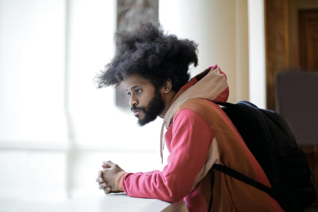 Portrait of a young man with an afro hairstyle looking contemplative indoors, wearing a backpack.