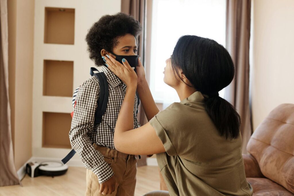 A mother helps her young son wear a face mask, creating a touching family moment indoors.