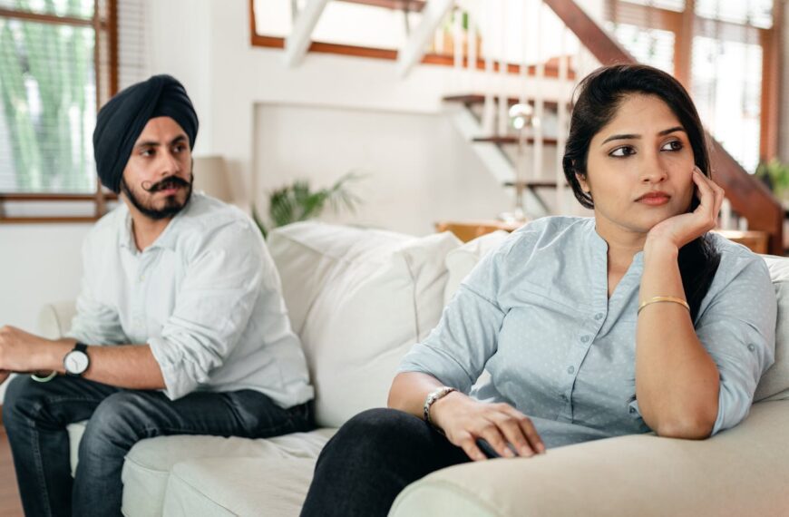 Resentful young Indian lady in casual wear ignoring husband in traditional turban during arguing at home