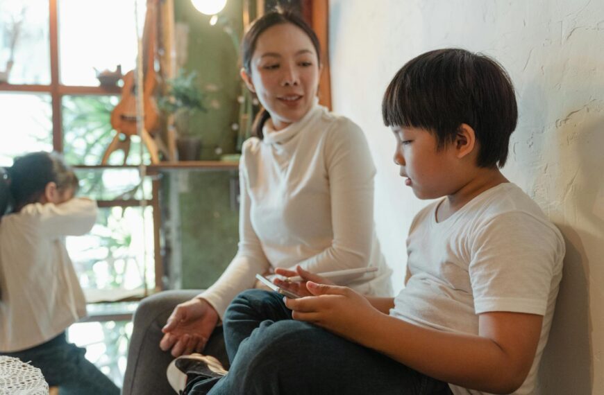 Positive ethnic woman sitting near cute son using tablet against adorable daughter looking at window while spending free time together at home