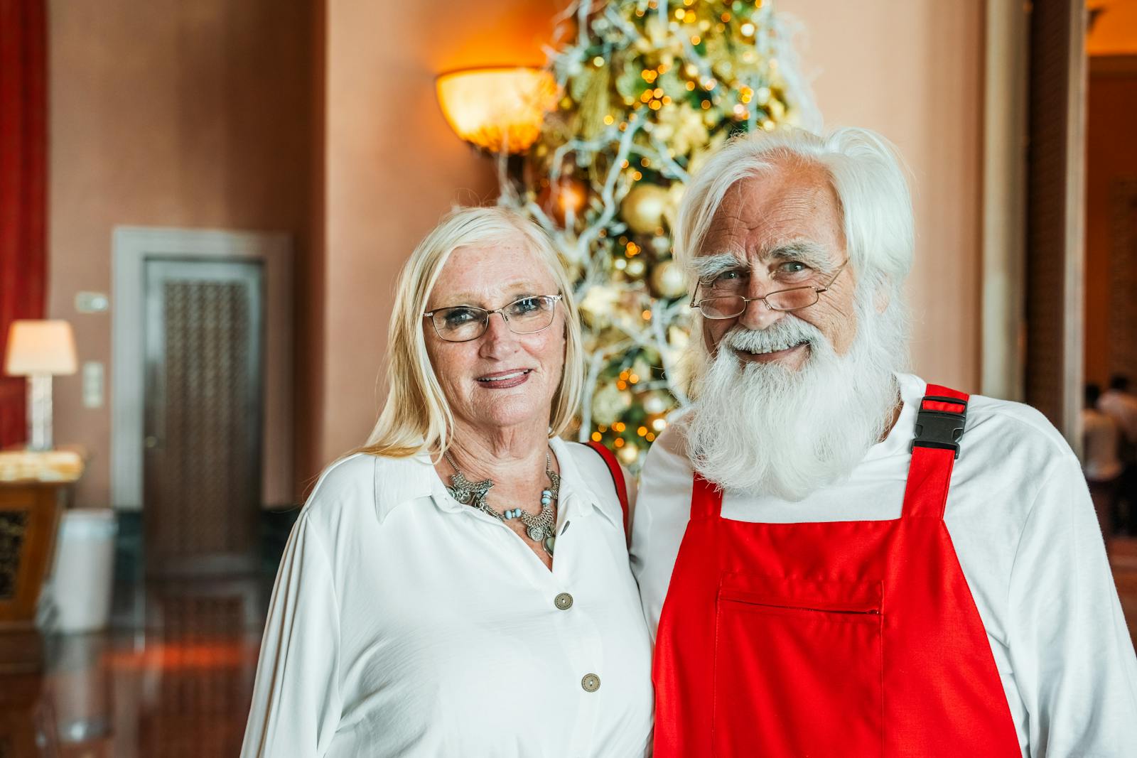 Senior couple smiling in front of a Christmas tree indoors in Dubai, United Arab Emirates.
