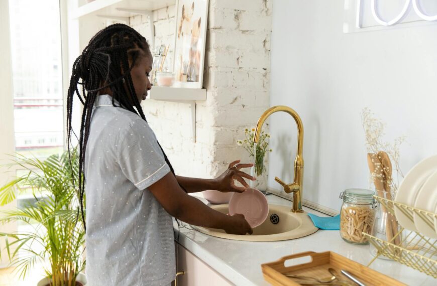 An adult woman washing dishes in a bright, modern kitchen setting.