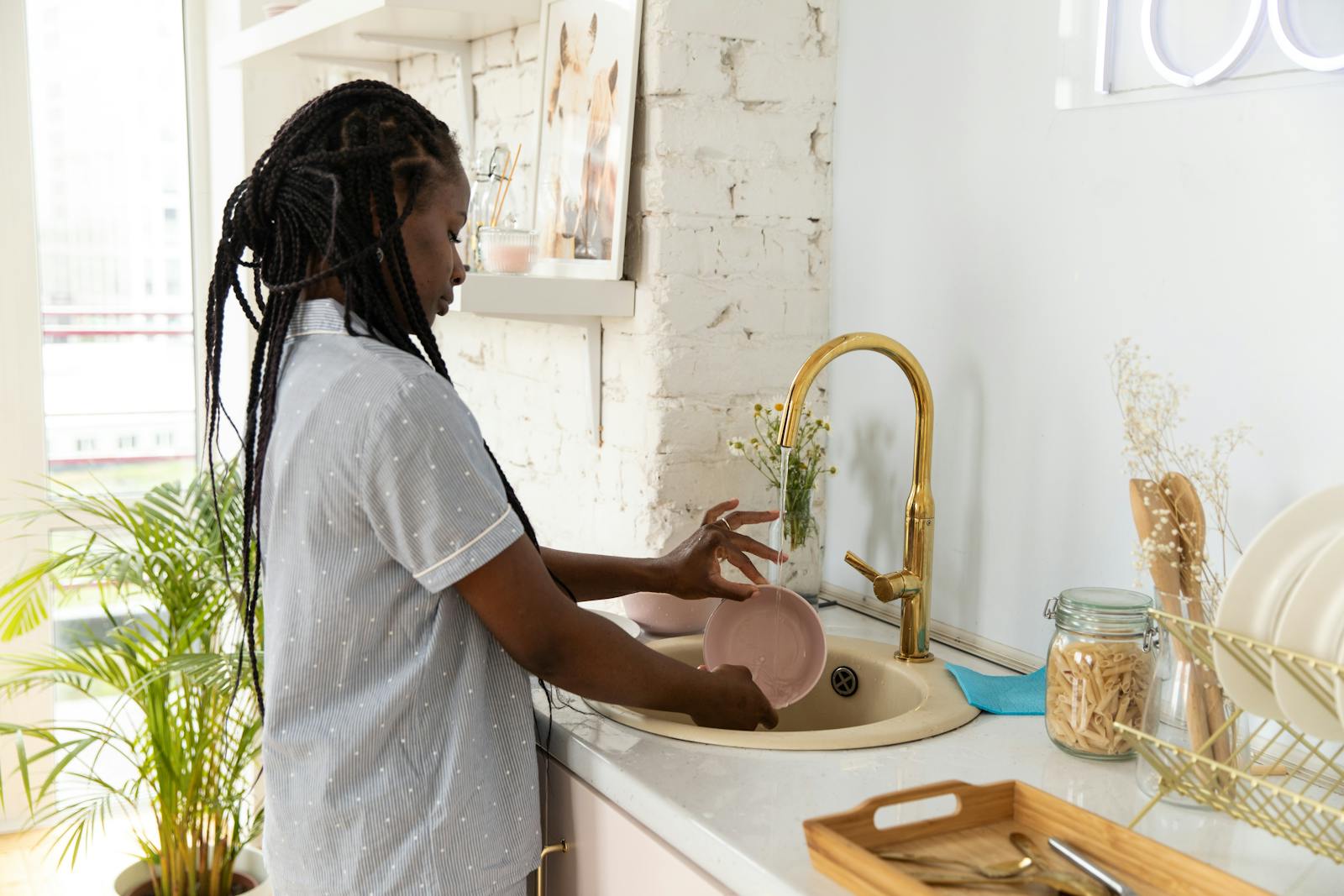 An adult woman washing dishes in a bright, modern kitchen setting.