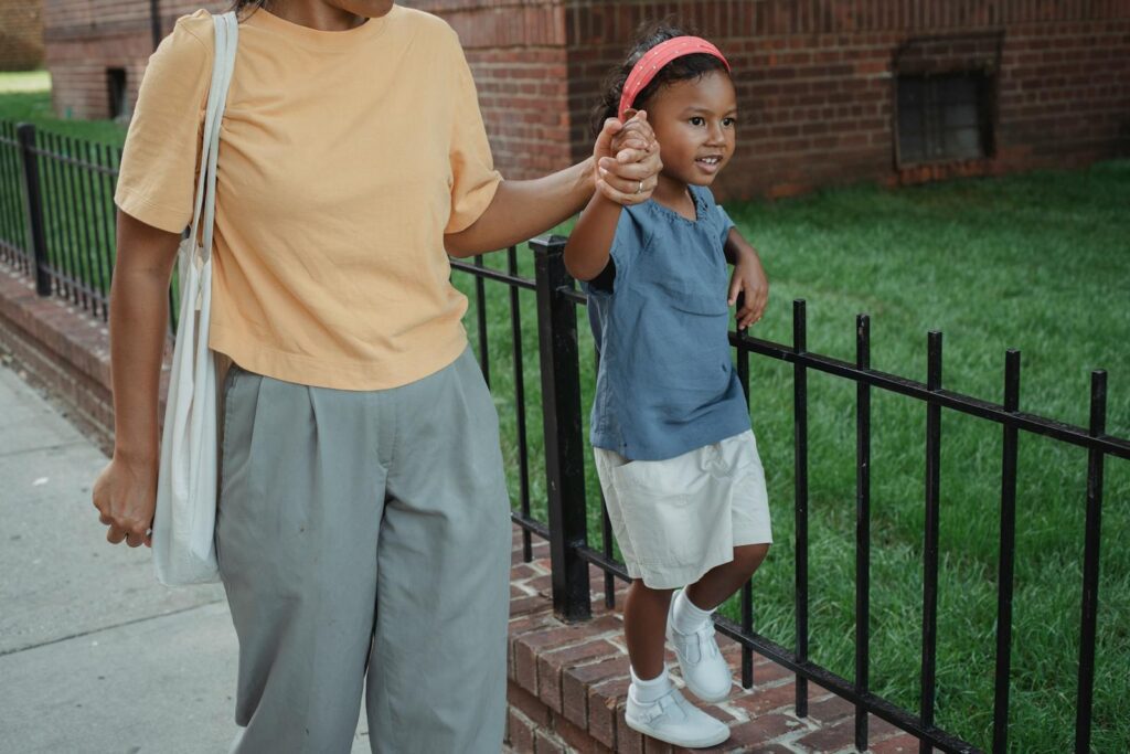High angle of Asian smiling daughter holding hand of mother while strolling together near fence