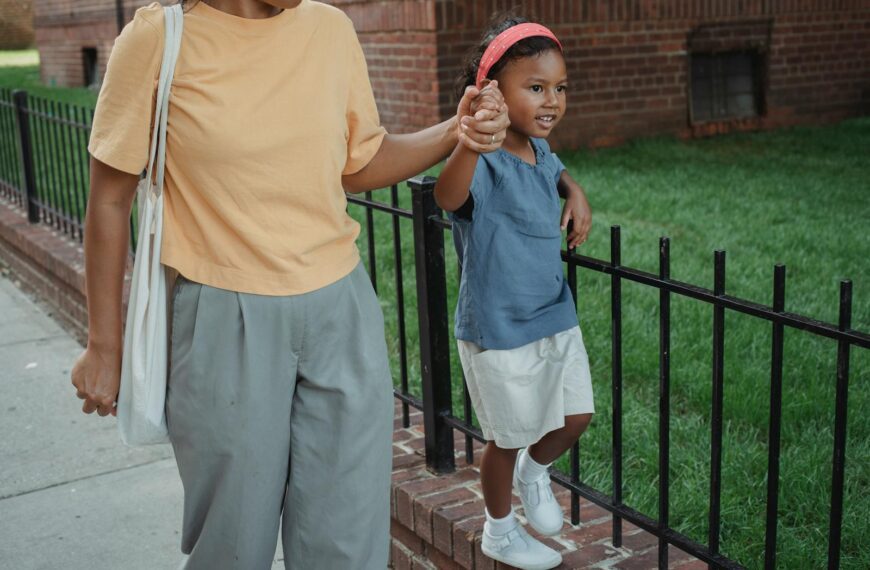 High angle of Asian smiling daughter holding hand of mother while strolling together near fence