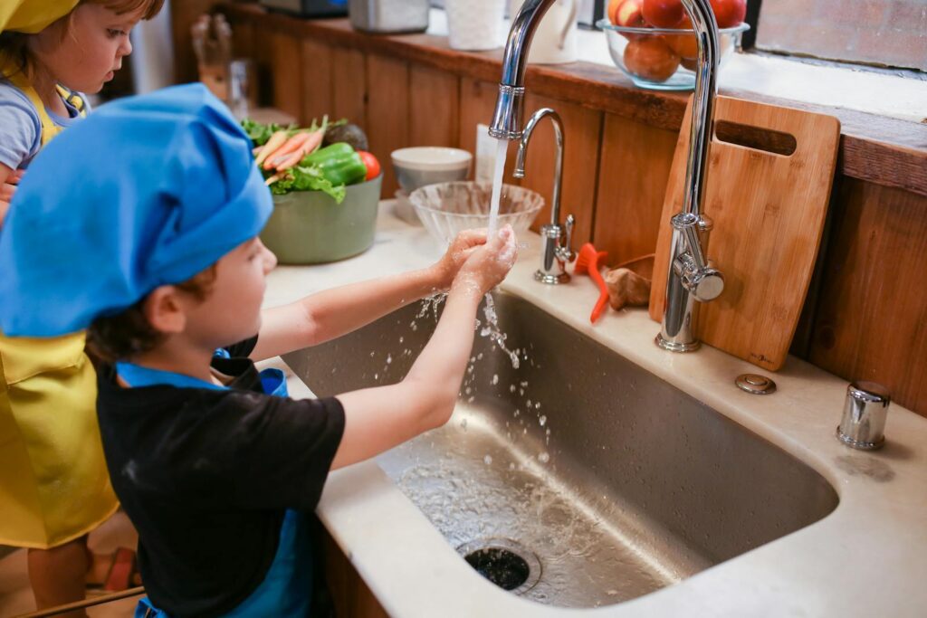 Children learning to cook and practicing hygiene by washing hands in the kitchen.