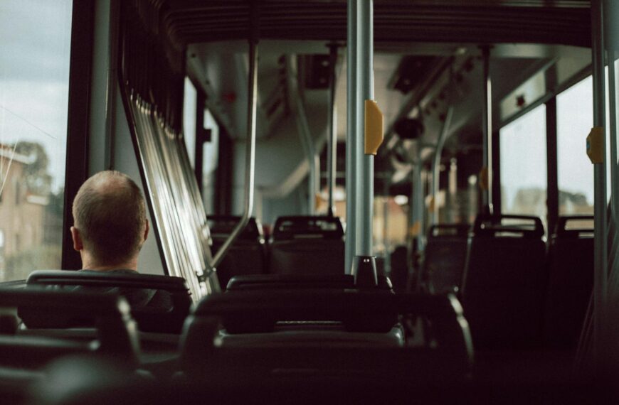 Back view of anonymous male riding on empty bus while sitting on passenger seat near window during trip in city street