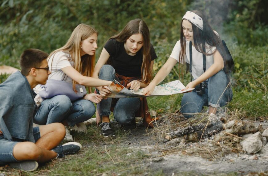 Group of teens sitting around a campfire, planning adventure with a map.