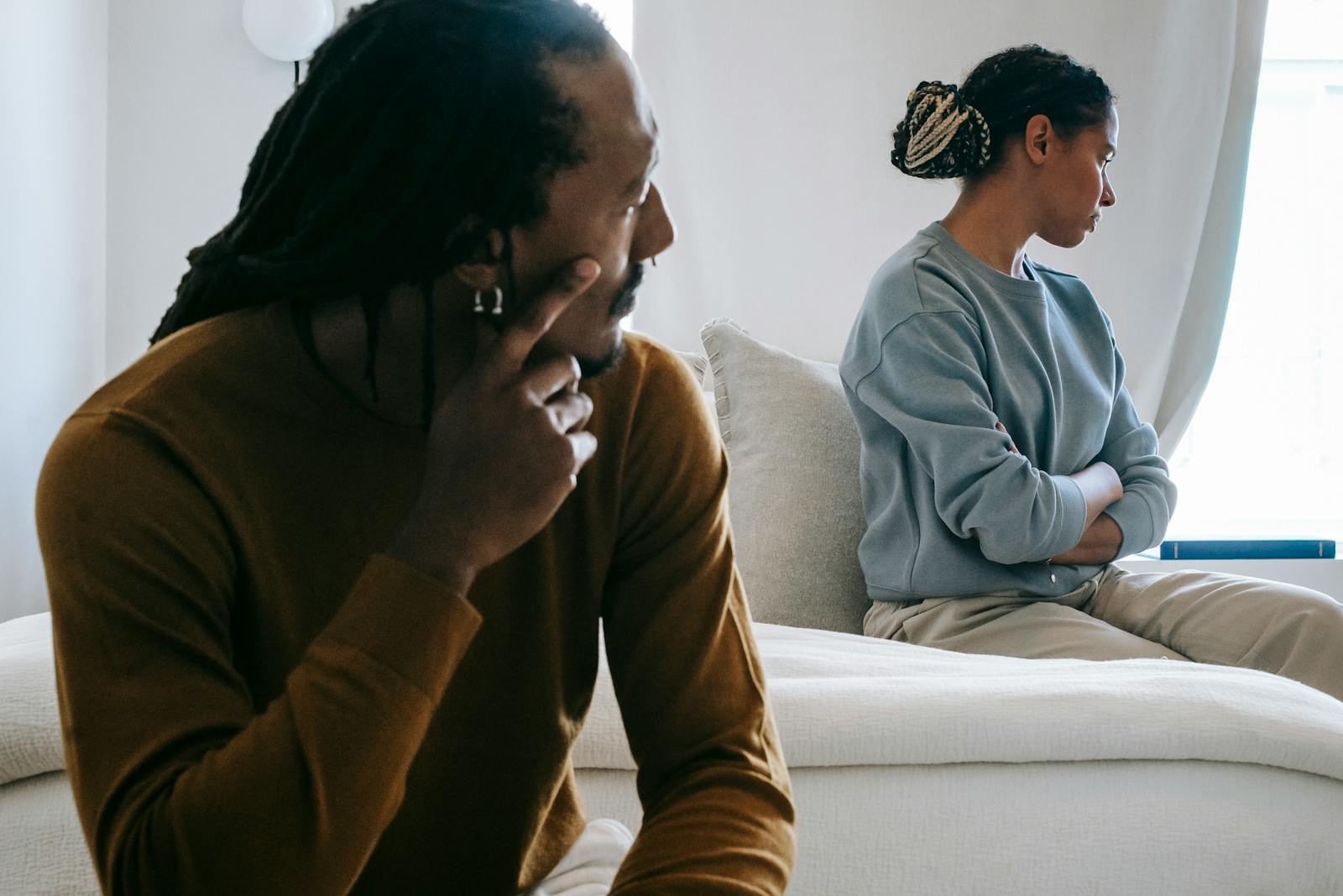 Young African American couple sitting on bed with sad face in casual outfit and thinking at home
