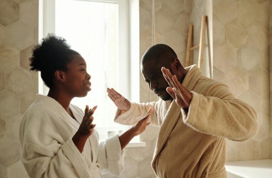 A couple in bathrobes having an emotional discussion in an indoor setting with expressive hand gestures.