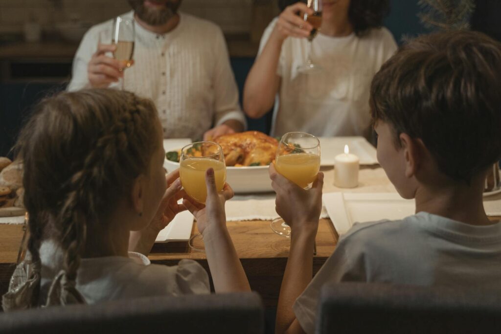 Two children and adults together at a cozy family dinner table, raising glasses in a toast.