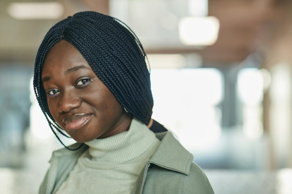 Close-up of a smiling woman with braided hair wearing a turtleneck sweater indoors.