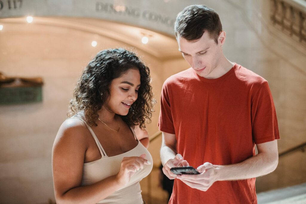 Young multiracial male and female friends in casual outfits browsing smartphone while standing together in university corridor during break