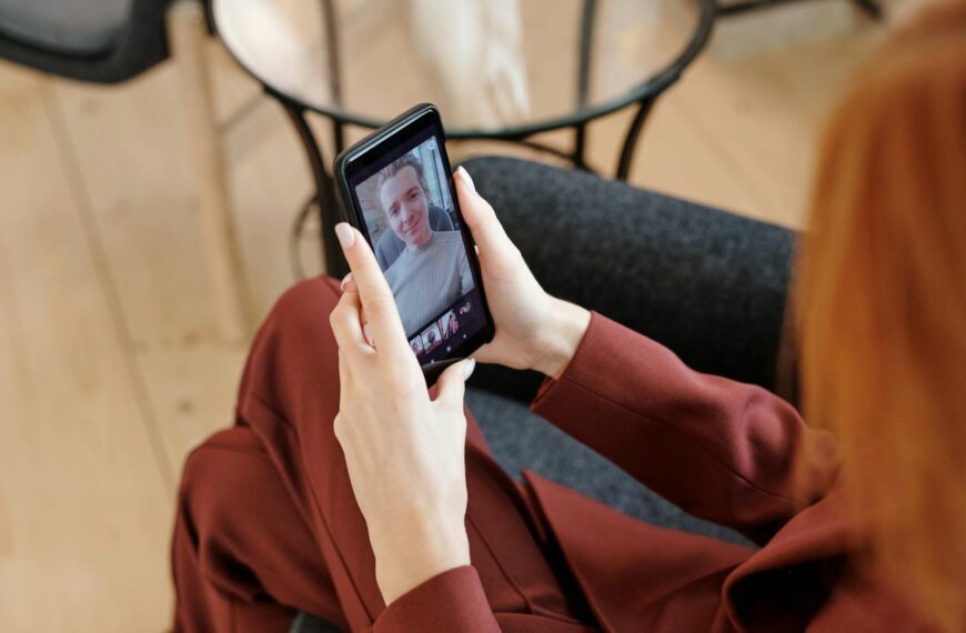 Woman in red suit video calling on smartphone, indoor setting.