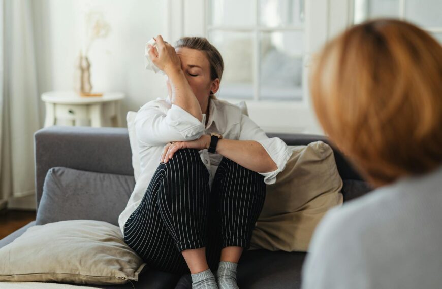 A woman wipes tears during a therapy session on a couch indoors.