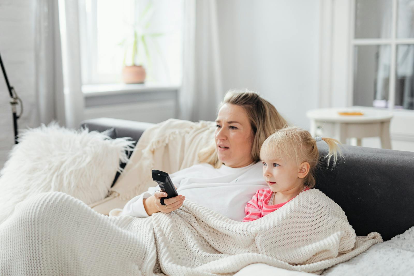 A mother and daughter cuddled on the couch under a blanket, enjoying TV time.