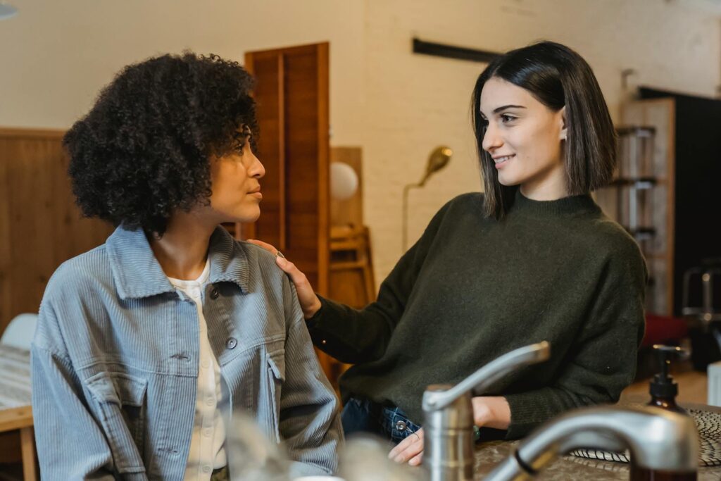 Positive female stroking shoulder of upset African American female friend with Afro hairdo and looking at each other