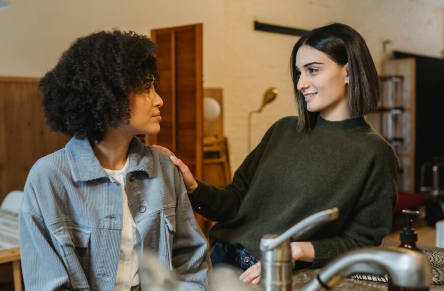 Positive female stroking shoulder of upset African American female friend with Afro hairdo and looking at each other