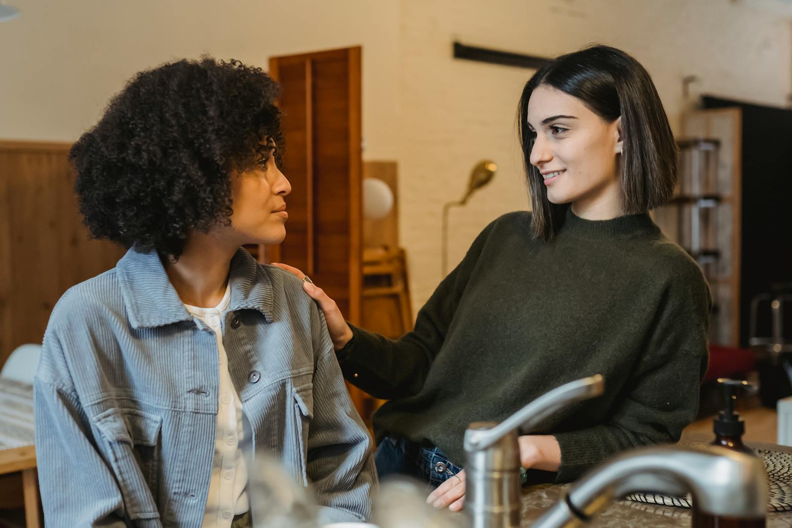 Positive female stroking shoulder of upset African American female friend with Afro hairdo and looking at each other