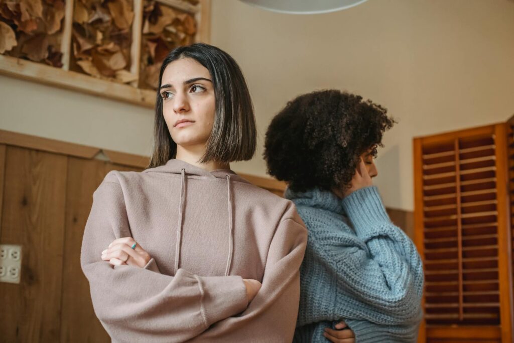 From below of unsatisfied multiracial women in casual clothes with crossed arms standing in light room during quarrel at home