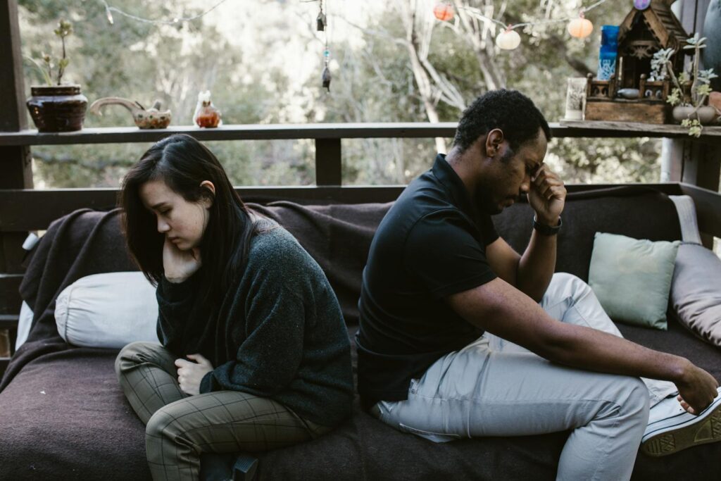 Interracial couple sitting back to back, reflecting emotional conflict, outdoors.