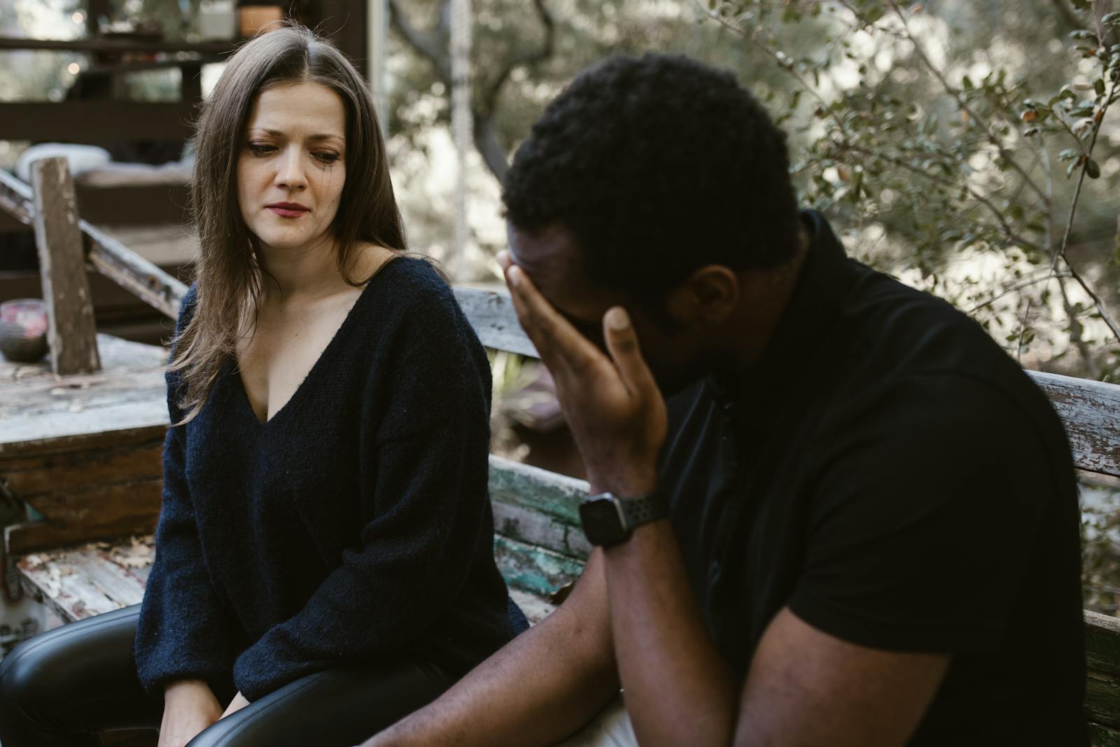 A couple experiencing emotional tension during a conversation outside on a bench.