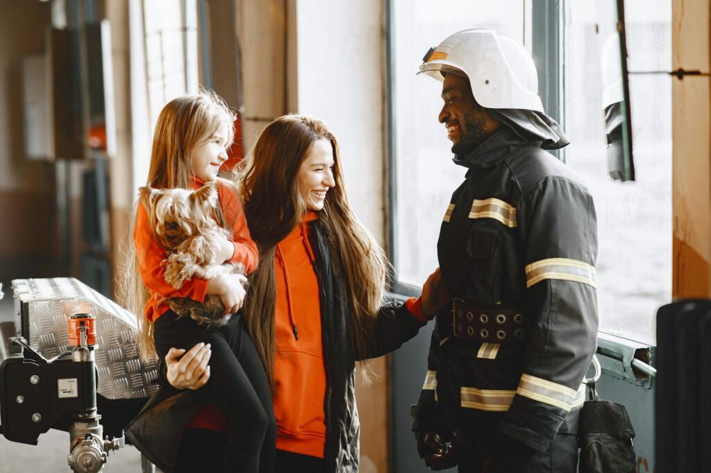 A mother and daughter share a joyful moment with a friendly firefighter inside the station.