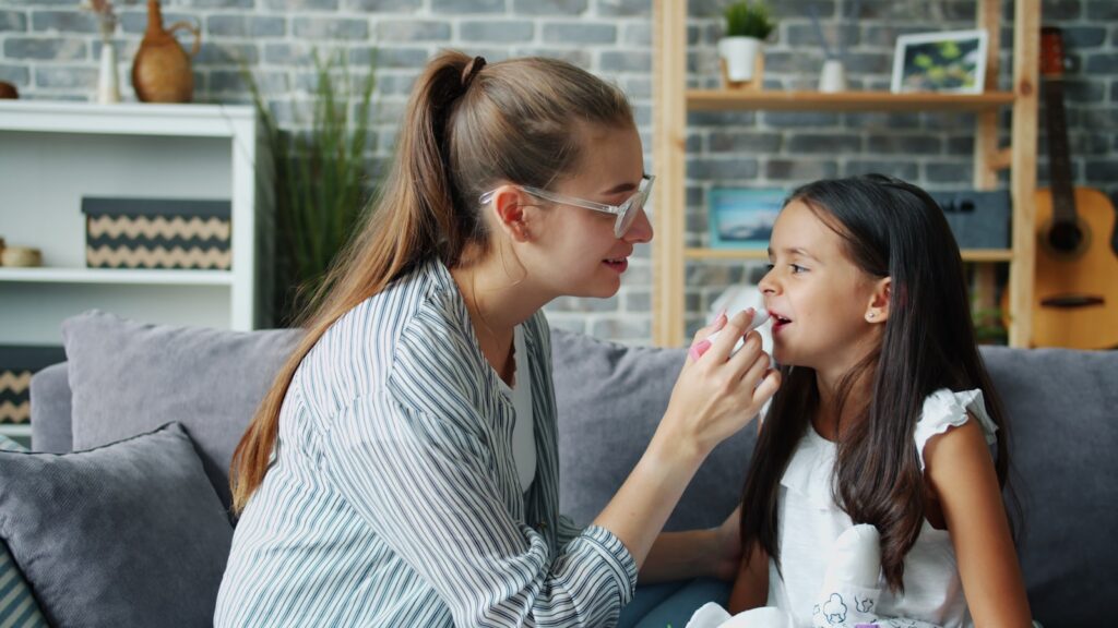 Mother wiping daughter's nose with tissue on sofa
