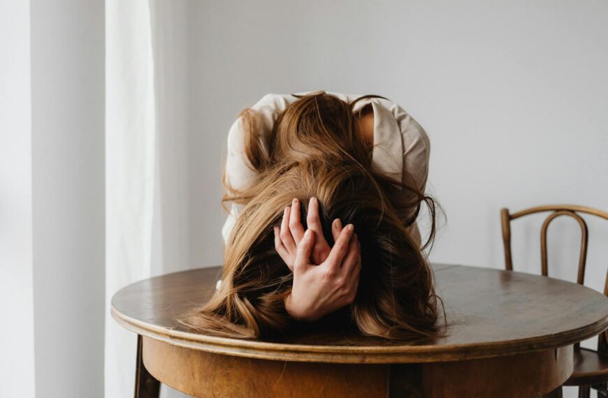 A woman showing despair with her head down on a table, indicating stress.